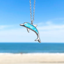 Load image into Gallery viewer, Ocean Treasure Sand Dolphin Necklace hanging close for a shot with a blurred beach background.