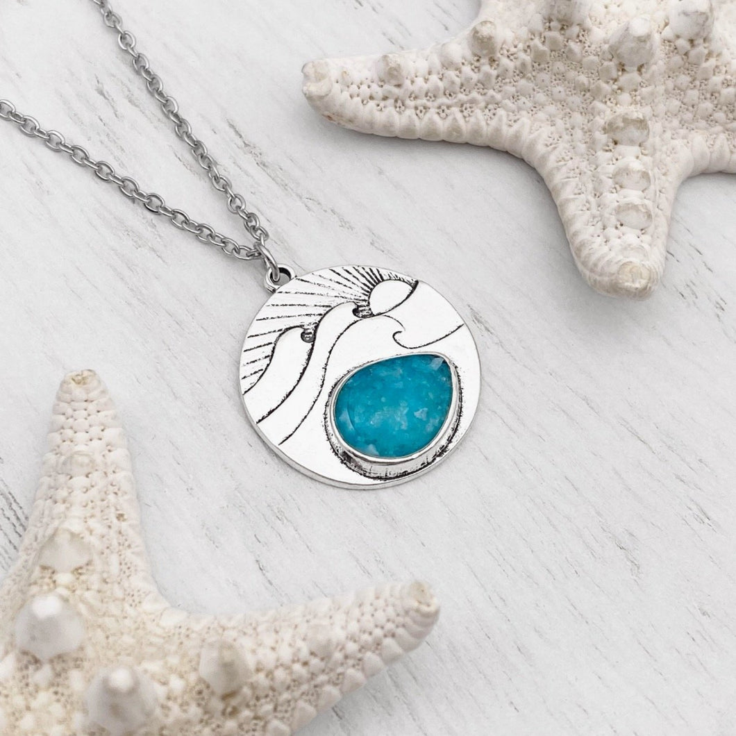 Ocean Treasure Sand Wave Necklace is positioned on top of a white wooden surface.