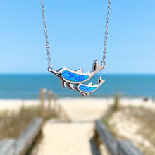 Load image into Gallery viewer, Opal Dolphin Duo Necklace hanging for a close-up shot with a beach background blurred. 