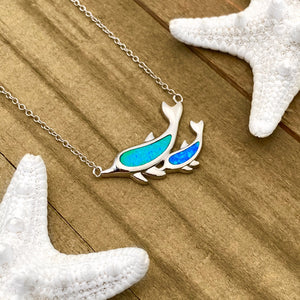 Opal Dolphin Duo Necklace displayed on a wooden surface.