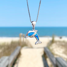 Load image into Gallery viewer, Opal Dolphin Necklace hanging close for a shot with a blurred beach background.