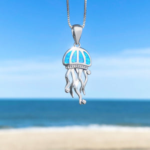 The Opal Don't Be Jelly Necklace is hanging up close with a blurry beach background.