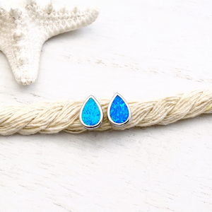 Opal Droplet Stud Earrings placed on a thick rope atop a white wooden surface.