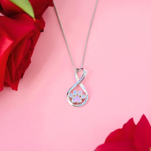 Load image into Gallery viewer, Opal Infinity Love Paw Necklace in Pink displayed on top of a pink surface with roses on the edge of the shot.