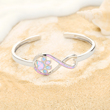 Load image into Gallery viewer, Opal Infinity Love Paw Cuff Bracelet in Pink, captured in a close-up shot on a beach shore.