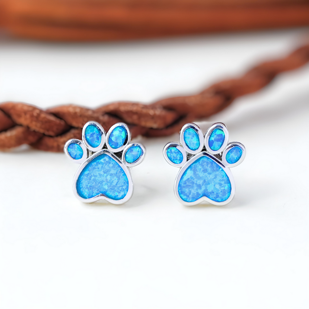 Opal Love Paw Studs displayed on a white surface with a brown leash at the back.