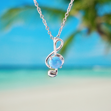 Load image into Gallery viewer, Opal Music Note Necklace hanging close for a shot with a blurred beach background.