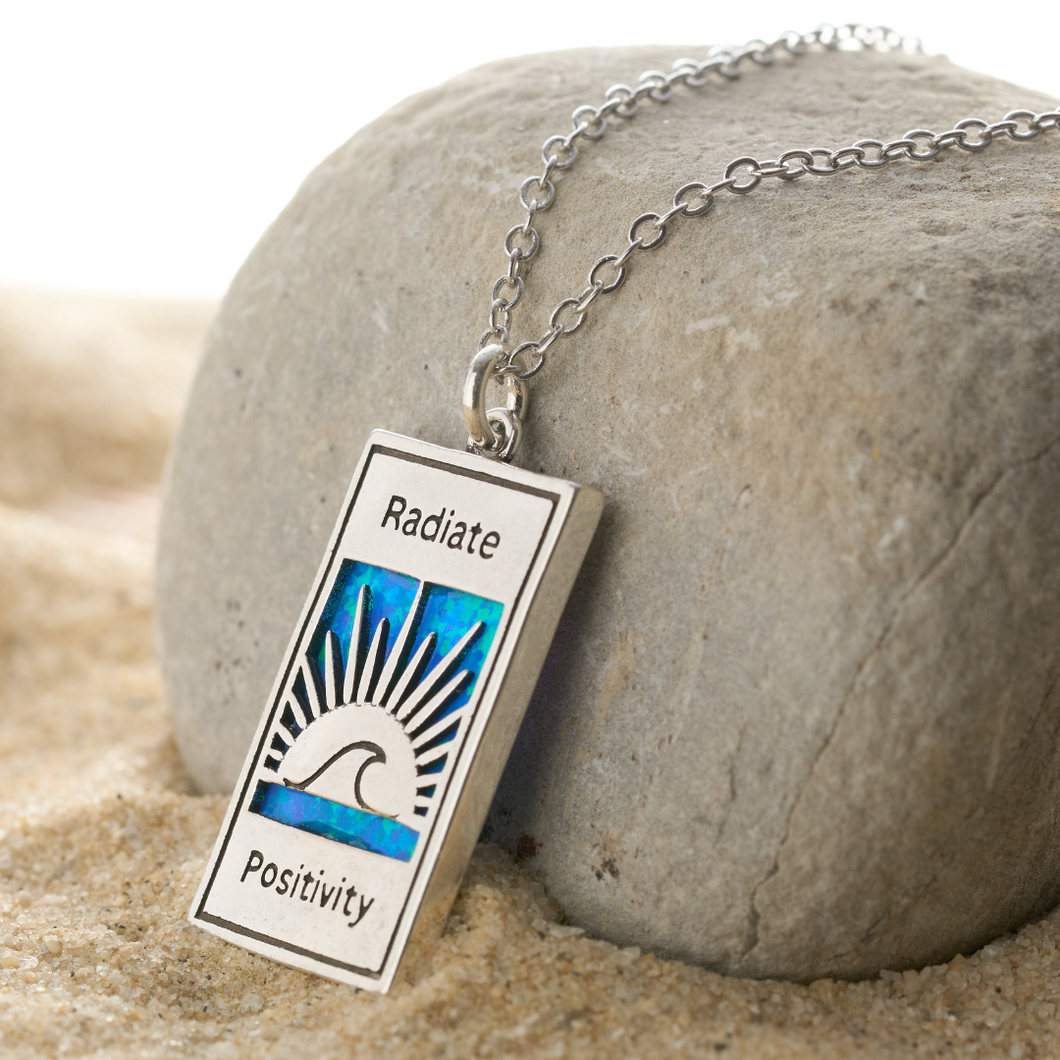 Opal Radiate Positivity Necklace is leaning on a big rock while on a sandy environment.