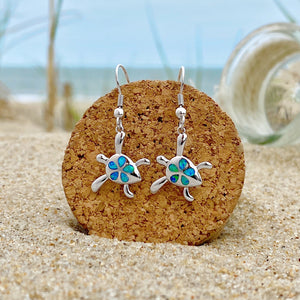 Opal Sea Turtle Flower Earrings displayed on a cork on a sandy beach, perfect for ocean-inspired accessories.
