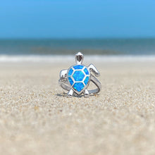 Load image into Gallery viewer, Opal Swimming Sea Turtle Ring is showcased on the sandy shore against a blurred beach background.