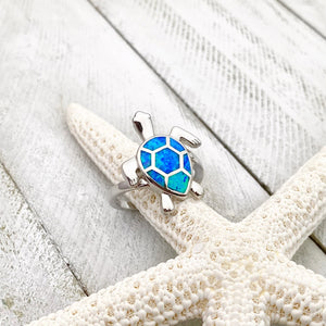 Opal Swimming Sea Turtle Ring displayed by being placed on a dried artificial starfish.