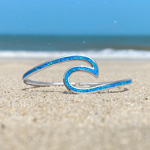 Opal Wave Cuff Bracelet displayed on a sandy shore with a blurred beach background.