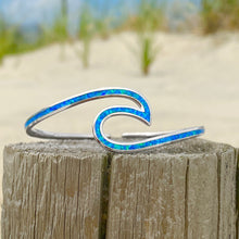 Load image into Gallery viewer, Opal Wave Cuff Bracelet is placed on top of a wooden log with a blurred beach background.