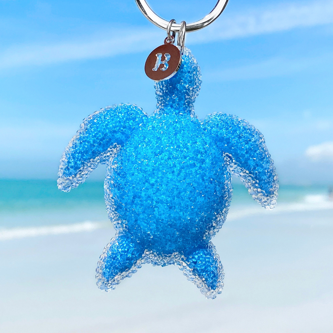 Playful Sea Turtle Keychain hanging close for a shot with a blurred beach background.