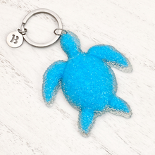 Load image into Gallery viewer, Playful Sea Turtle Keychain displayed on a white wooden surface.