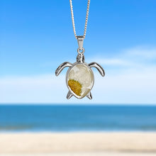 Load image into Gallery viewer, Pressed Daisy Sea Turtle Necklace hanging against a blurred beach background, perfect for beach-themed accessories.