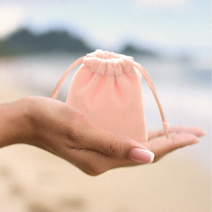 Rosy Velvet Jewelry Bag is displayed by being placed on a woman's hand with a blurred beach background.