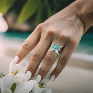 Sand Sea Star Ring displayed by being worn on a woman's hand as she reaches for a white flower.