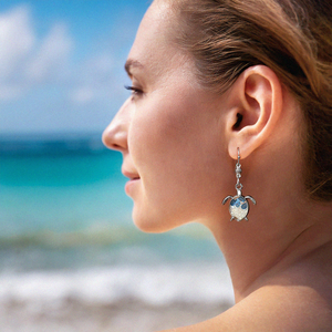 Sand Sea Turtle Earrings displayed by being worn on a woman's ear at the beach.