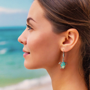 Sand Sea Turtle Earrings displayed by being worn on a woman's ear at the beach.