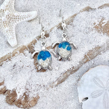 Load image into Gallery viewer, Sand Sea Turtle Earrings are displayed by being placed on top of a sand covered driftwood.