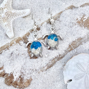 Sand Sea Turtle Earrings are displayed by being placed on top of a sand covered driftwood.