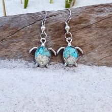 Load image into Gallery viewer, Sand Sea Turtle Earrings are displayed by being placed on top of a driftwood on the sand.