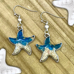 Sand Starfish Earrings in Blue Glass are displayed on a wooden surface.