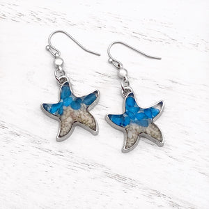Sand Starfish Earrings in Blue Glass are displayed on a white wooden surface.