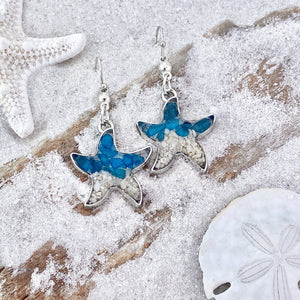 Sand Starfish Earrings in Blue Glass are displayed by being placed on top of a sand covered driftwood.