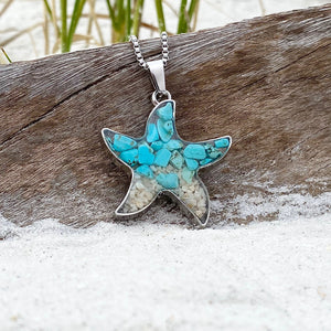 Sand Starfish Necklace in Teal Turquoise is displayed by being placed on top of a driftwood on the sand.