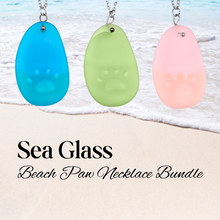 Load image into Gallery viewer, Necklaces being hung up close with a beach background and text that reads &#39;Sea Glass Beach Paw Necklaces.&#39;