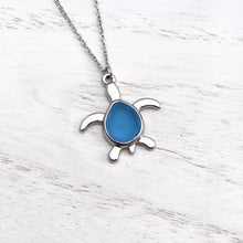 Load image into Gallery viewer, Sea Glass Sea Turtle Necklace in Sky Blue is displayed on a white wooden surface.
