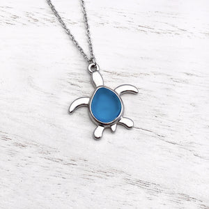 Sea Glass Sea Turtle Necklace in Sky Blue is displayed on a white wooden surface.