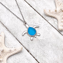 Load image into Gallery viewer, Sea Glass Sea Turtle Necklace in Sky Blue is displayed on a white wooden surface.