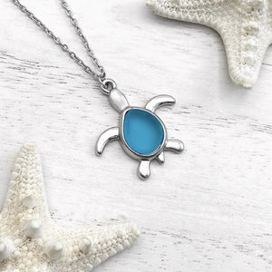 Sea Glass Sea Turtle Necklace in Sky Blue is displayed on a white wooden surface.