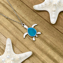 Load image into Gallery viewer, Sea Glass Sea Turtle Necklace in Sky Blue is displayed on a wooden surface.