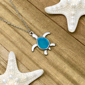Sea Glass Sea Turtle Necklace in Sky Blue is displayed on a wooden surface.
