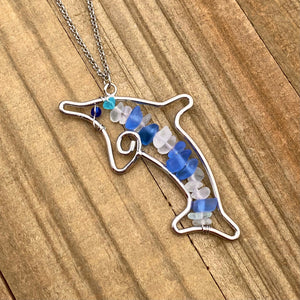 Stacked Sea Glass Dolphin Necklace displayed on a wooden surface.