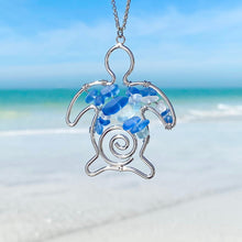Load image into Gallery viewer, The Stacked Sea Glass Sea Turtle Necklace is hanging up close with a blurred beach background.