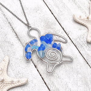 The Stacked Sea Glass Sea Turtle Necklace is displayed on a white wooden surface.