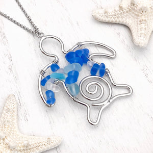 he Stacked Sea Glass Sea Turtle Necklace is displayed on a white wooden surface.
