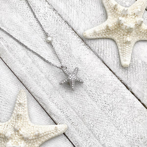 Starfish Hidden Pearl Necklace displayed on a white wooden surface.