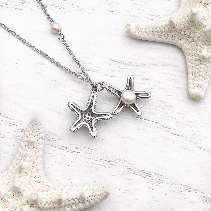 Starfish Hidden Pearl Necklace displayed on a white wooden surface.