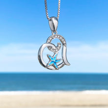 Load image into Gallery viewer, Starfish Love Necklace hanging close for a shot with a blurred beach background.