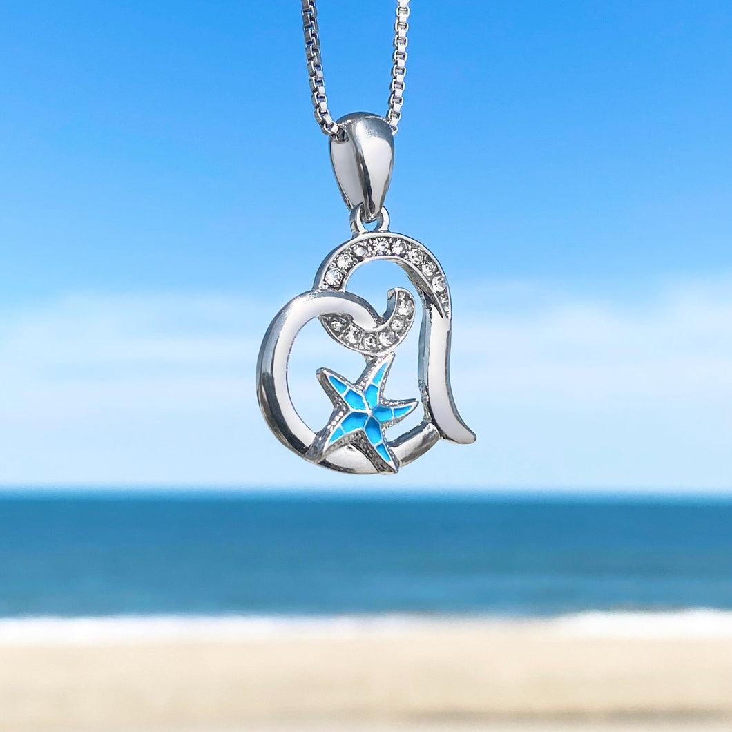 Starfish Love Necklace hanging close for a shot with a blurred beach background.