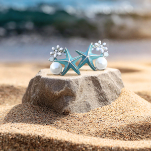 Starfish Pearl Studs are placed on top of a stone slab that is partially buried in the shore sand.