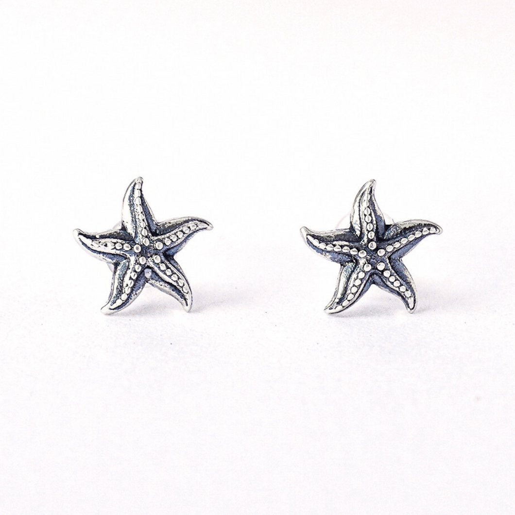 Sterling Silver Dancing Starfish Studs are displayed on a rough white surface.