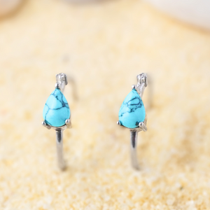 Turquoise Droplet Hoop Earrings are displayed by being placed on the sand.