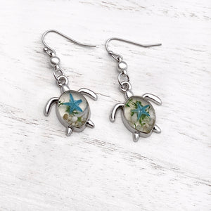 Deep in the Ocean Sea Turtle Earrings displayed on a white wooden surface.